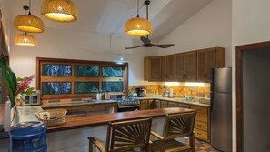 A kitchen with wooden cabinets, a refrigerator, a stove, and a dining area with chairs.