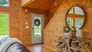 Un interior de madera con una puerta, un espejo redondo y una mesa de madera con plantas.