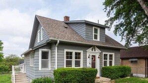 A two-story house with a front porch, a chimney, and a small front yard with a hedge. - Modern Midtown Getaway! Central location for 12! (Omaha)