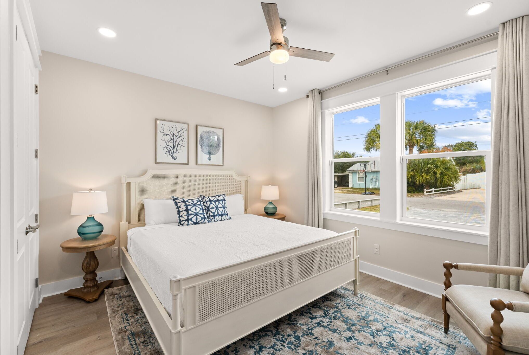 Une chambre à coucher comprenant un lit, deux tables de chevet, un ventilateur de plafond et une grande fenêtre donnant sur l’extérieur.