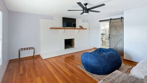 A room with a white brick fireplace, a ceiling fan, and a wooden floor.