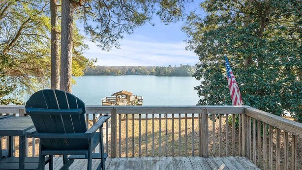 A wooden deck with a view of a lake, a dock, and an American flag.