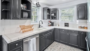 A modern kitchen with dark cabinetry, a white countertop, and a tiled backsplash.