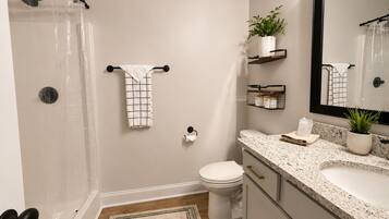 A bathroom with a shower, toilet, sink, and mirror.
