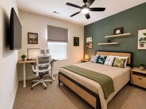 Un dormitorio con cama, escritorio, silla y ventilador de techo.