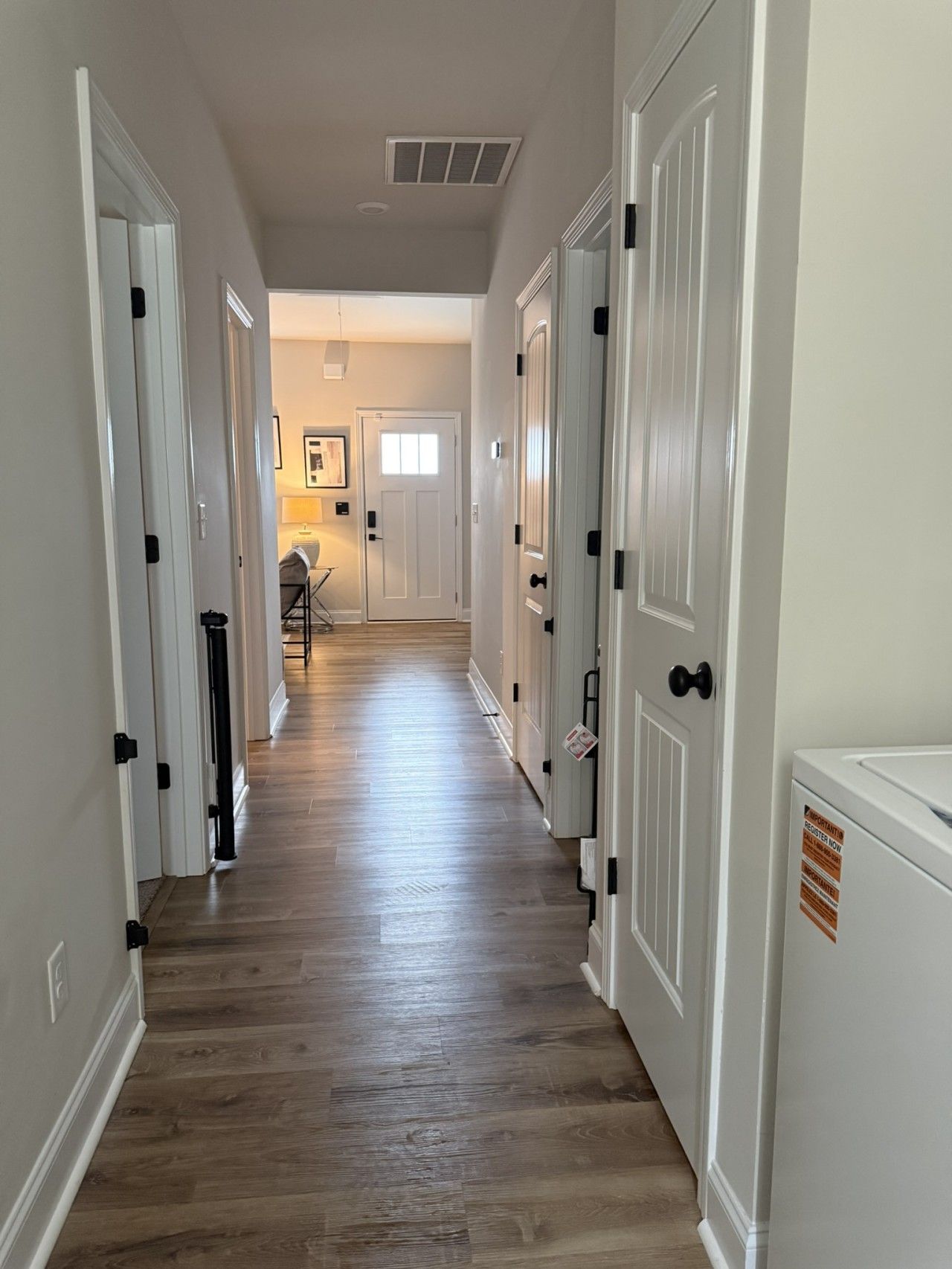 A hallway with wooden flooring, white doors, and a ceiling vent.