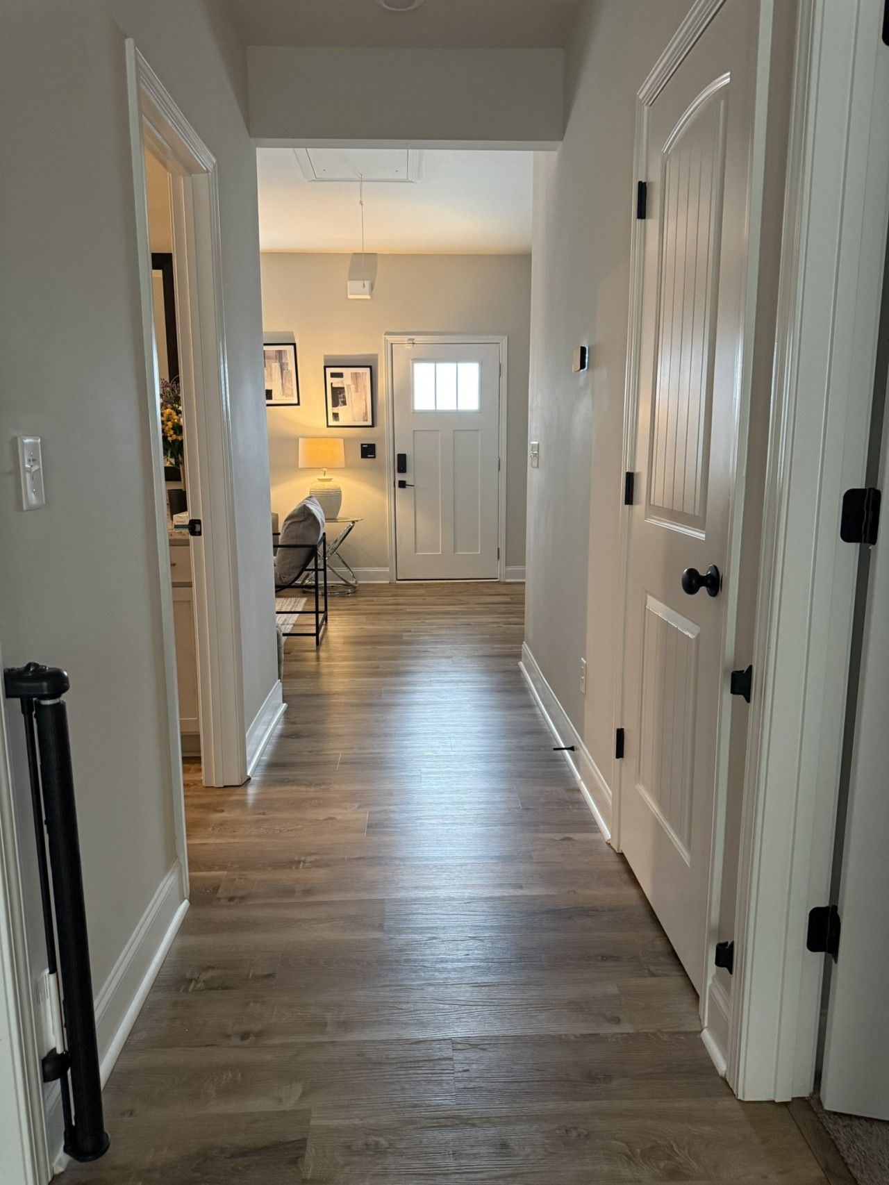 A hallway with wooden flooring, white walls, and doors with black handles.