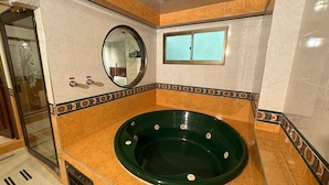 Un bagno con vasca idromassaggio verde, box doccia in vetro e bordatura decorativa in piastrelle.