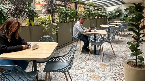 Un caffè all'aperto con pavimento piastrellato, sedie in metallo e piante in vaso.