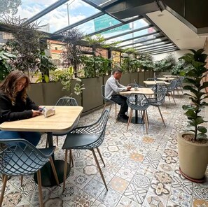An outdoor café with tiled flooring, metal chairs, and potted plants. - Lavid Hotel Palacio Real (Bogotá)