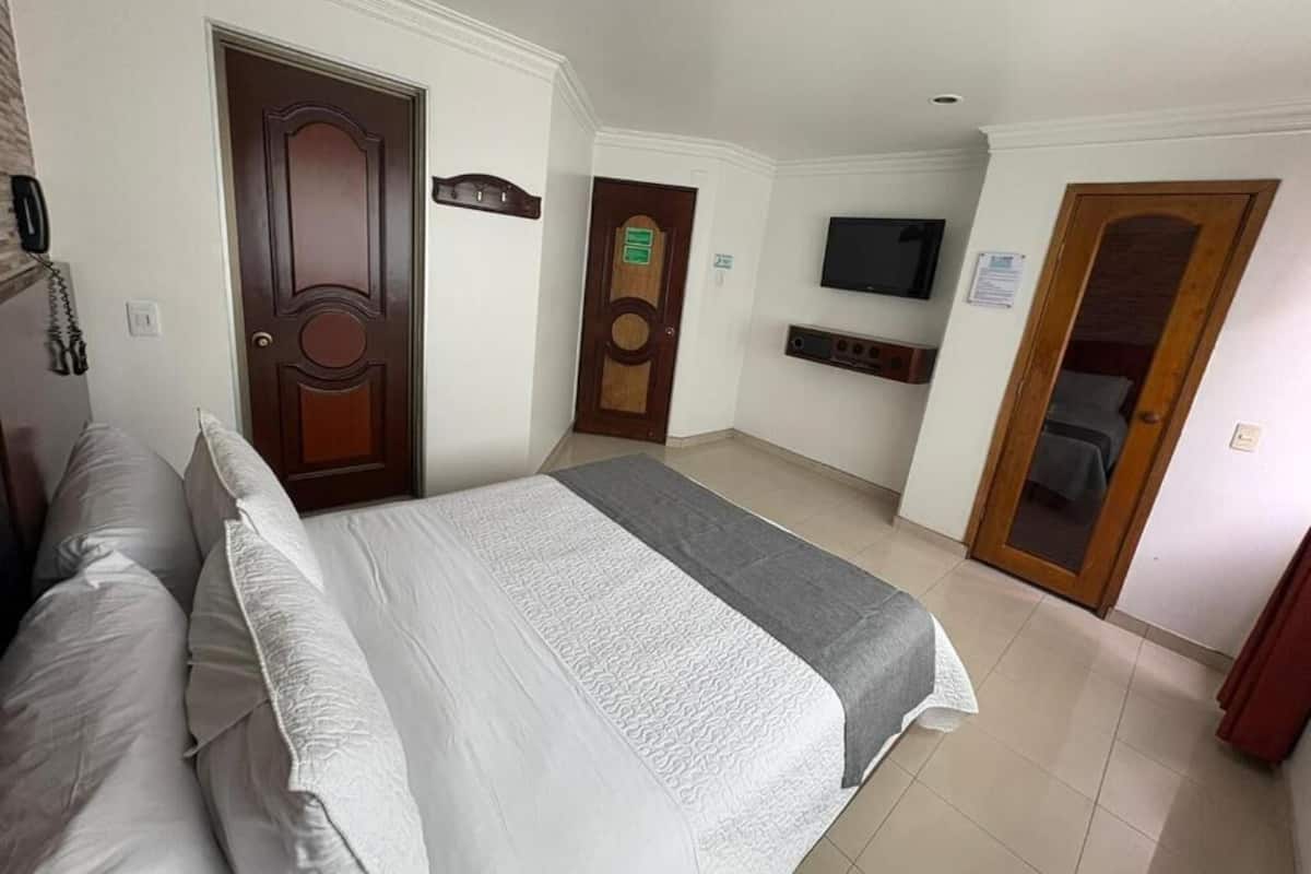 A hotel room with a bed, a television, a door, and a small desk area.