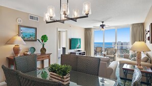 A spacious living room with a glass dining table, comfortable seating, a chandelier, and a view of the ocean. - Pelican Beach Terrace 1203 (Destin)