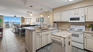 A modern kitchen with a central island, white cabinetry, and a large window overlooking the city. - Pelican Beach Terrace 1203 (Destin)