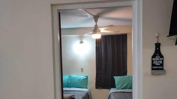 Habitación de hotel con dos camas, ventilador de techo y televisor montado en la pared.