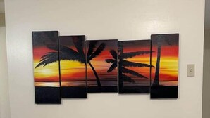 Un mur orné d’une œuvre d’art composée de trois panneaux représentant des palmiers se détachant sur un coucher de soleil.