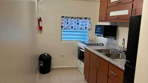 Une cuisine avec des meubles de rangement en bois, un réfrigérateur noir, un four à micro-ondes et une fenêtre agrémentée de rideaux à motifs.