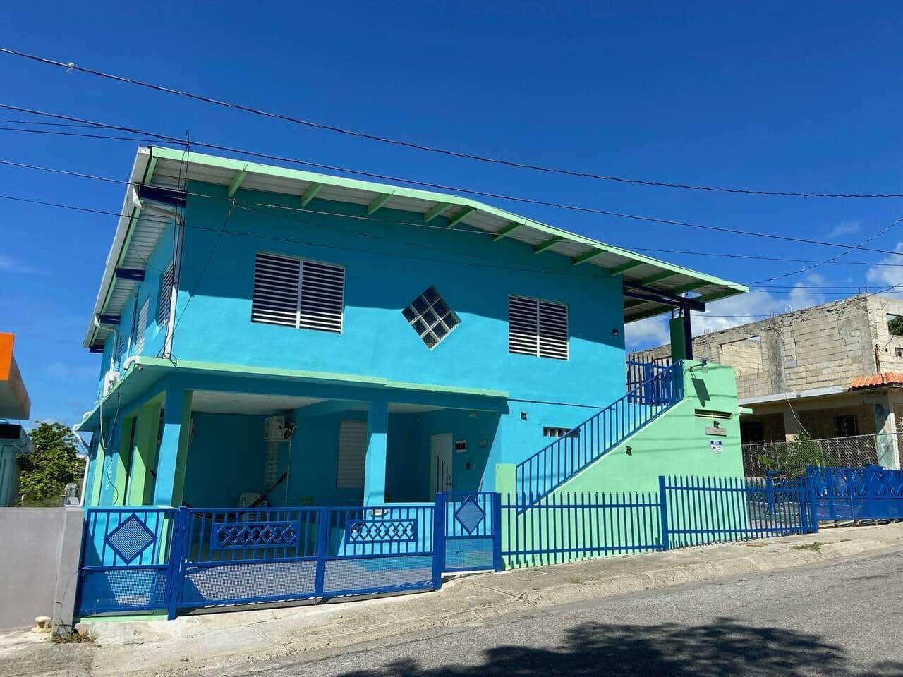 A two-story building with a blue exterior, a covered front porch, and a staircase leading to the upper floor.