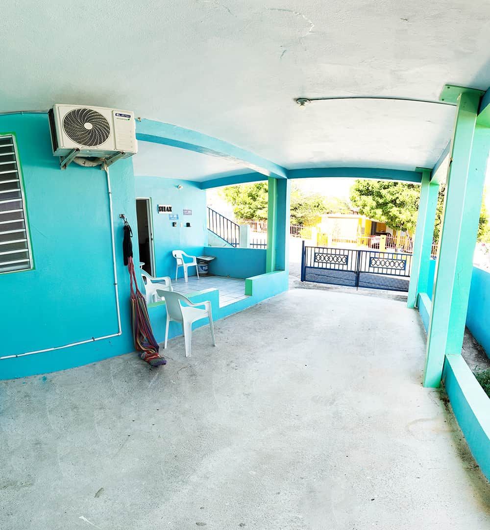 A covered outdoor area with a concrete floor, a blue wall, and a white air conditioning unit.
