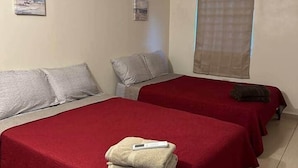 Habitación de hotel con dos camas, cada una con cubrecama y almohadas rojas, un pequeño cuadro en la pared y una ventana con cortina.