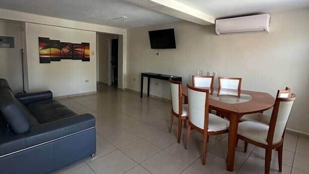 Una sala de estar moderna con un sofá azul, una mesa de comedor con sillas, un televisor de pantalla plana y un equipo de aire acondicionado.