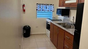 Una cocina con armarios de madera, un refrigerador negro, un microondas y una ventana con cortinas estampadas.
