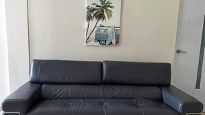 Un sofá de cuero negro en una habitación con suelo de baldosas y un cuadro colgado en la pared que muestra una escena de playa.