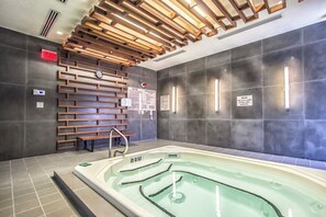 Un espace spa moderne doté d’un grand jacuzzi, d’un plafond en lambris de bois et de murs carrelés.