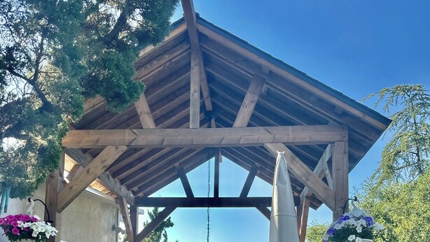 Een overdekt terras buiten met een houten pergola, een tafel met stoelen en een decoratieve fontein.