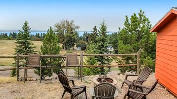 An outdoor seating area with Adirondack chairs and a fire pit, overlooking a scenic landscape with trees and a distant view of mountains.