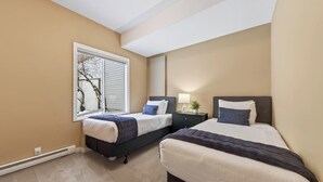 Camera da letto con due letti, una finestra e un comodino con lampada e pianta.