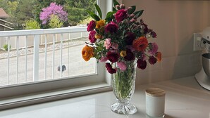 Une cuisine avec une grande fenêtre, un vase de fleurs et un tableau accroché au mur.