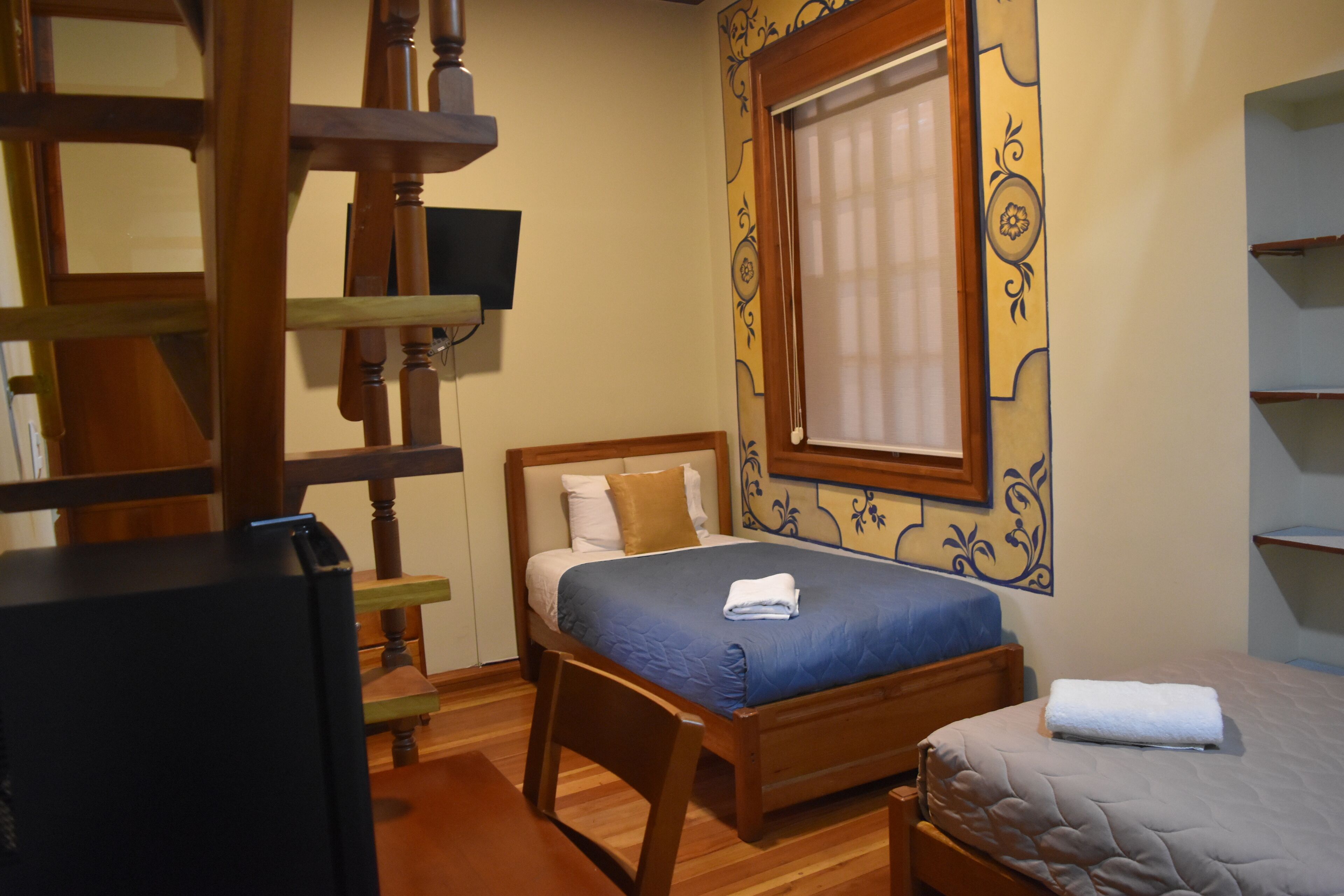 Una camera da letto con un letto e una scrivania in legno, una televisione e una finestra con cornice decorativa.