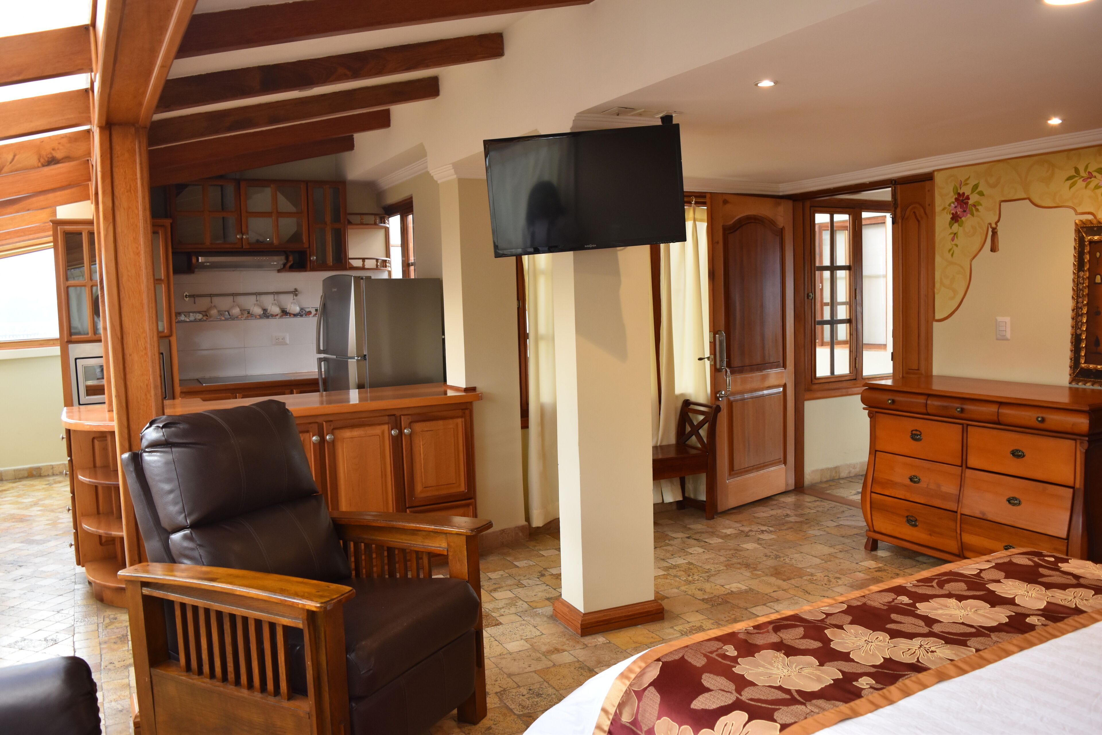 A room with a bed, wooden furniture, a television, and a kitchen area.