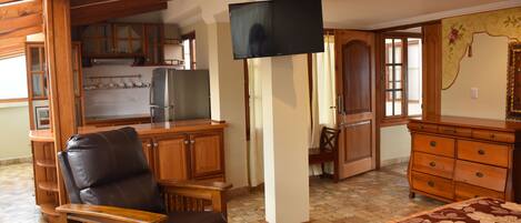 A room with a bed, wooden furniture, a television, and a kitchen area.