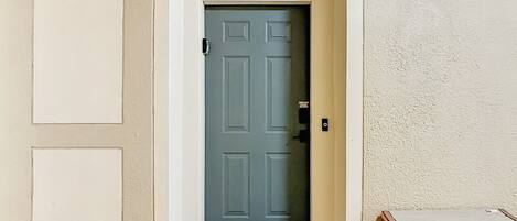 A hallway with a blue door, a welcome mat, and a sign above the door indicating the address.