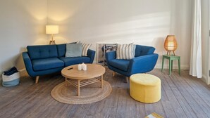A living room with a blue sofa set, a round wooden coffee table, a yellow ottoman, and a floor lamp. - 2 bedroom nice apartment in Skagen (Skagen)