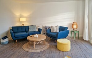 A living room with a blue sofa set, a round wooden coffee table, a yellow ottoman, and a floor lamp. - 2 bedroom nice apartment in Skagen (Skagen)