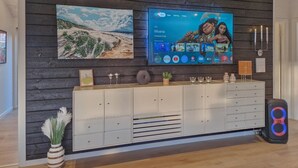Una sala de estar moderna con un televisor de pantalla plana montado en una pared de madera, un mueble blanco debajo y un altavoz grande en el suelo.