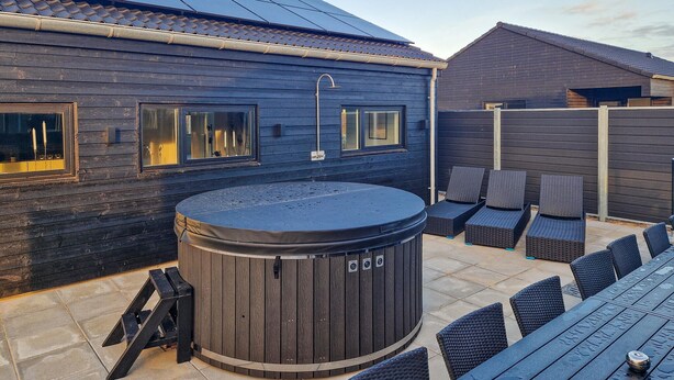 Un jacuzzi con revestimiento de madera, rodeado de mobiliario exterior y una pérgola.