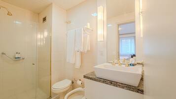 A bathroom with a glass shower enclosure, a toilet, a bidet, and a sink with gold faucets.