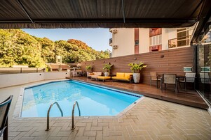 Piscina com deck de madeira, área de estar externa e vista para um morro.