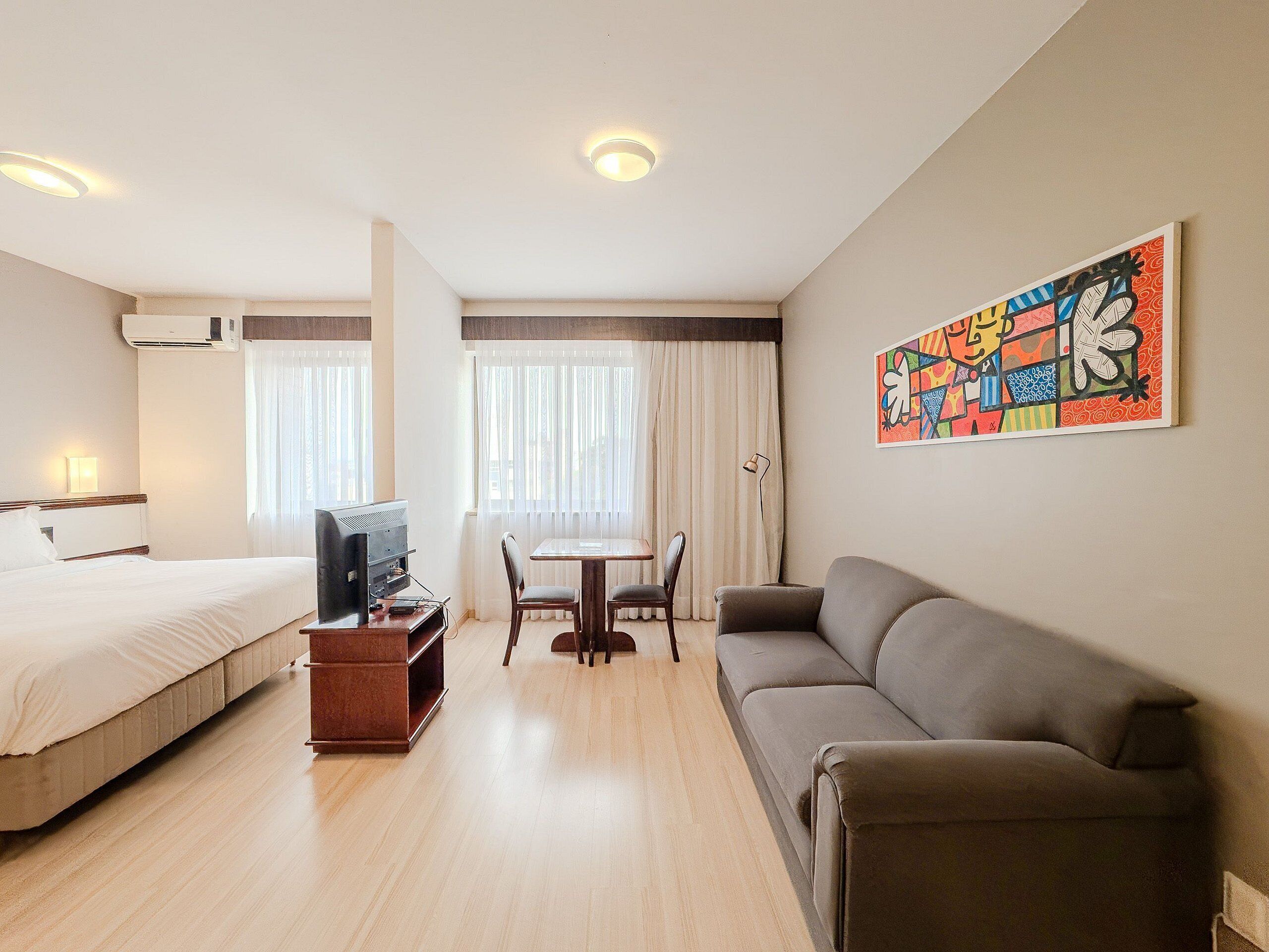 A hotel room with a bed, a sofa, a TV, a desk, and a chair.