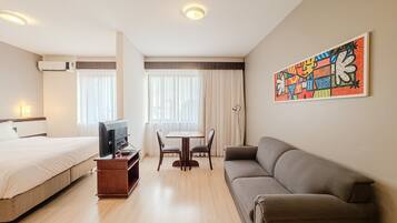 A hotel room with a bed, a sofa, a TV, a desk, and a chair.