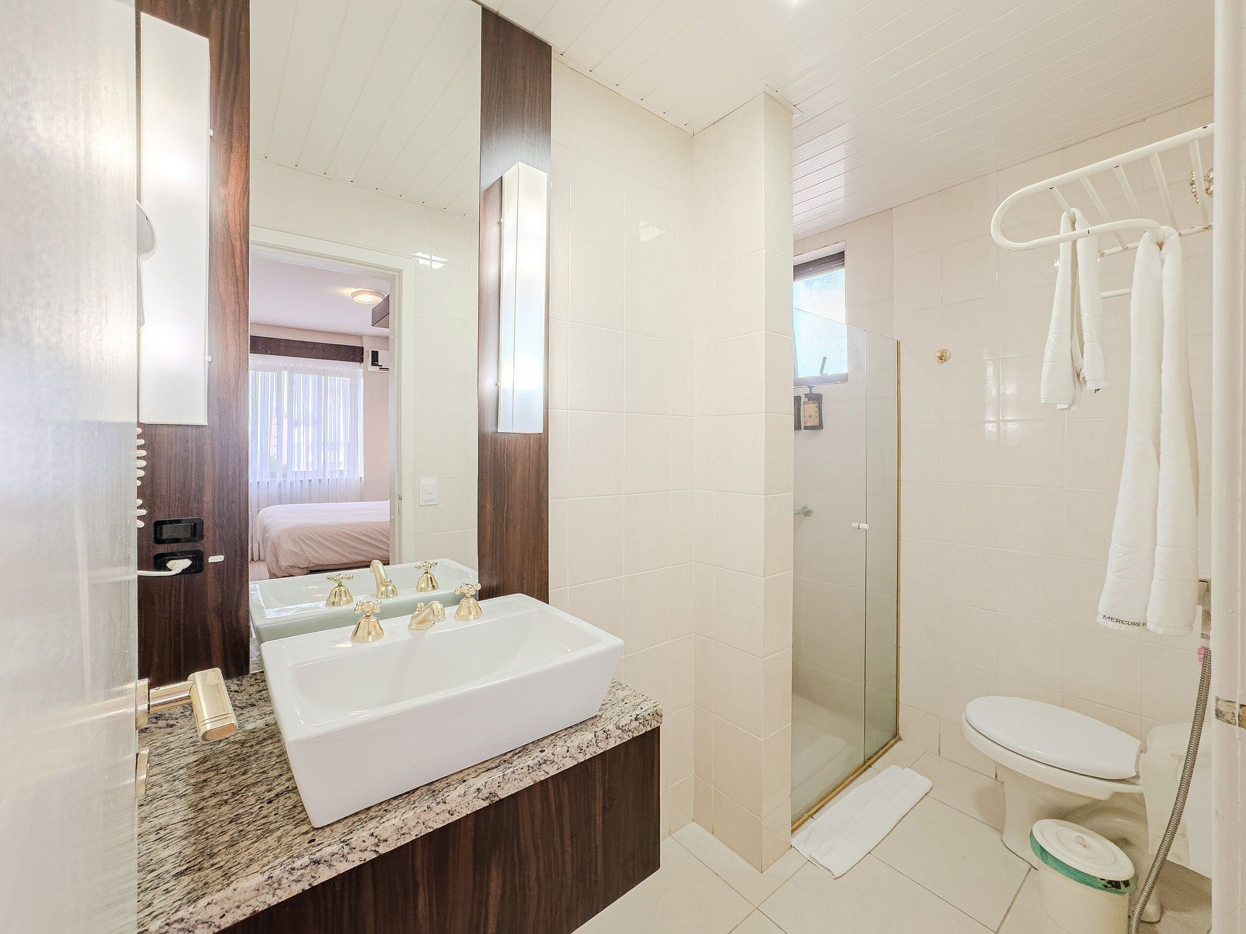 Une salle de bain moderne avec un grand miroir, un lavabo blanc, une douche et des toilettes.