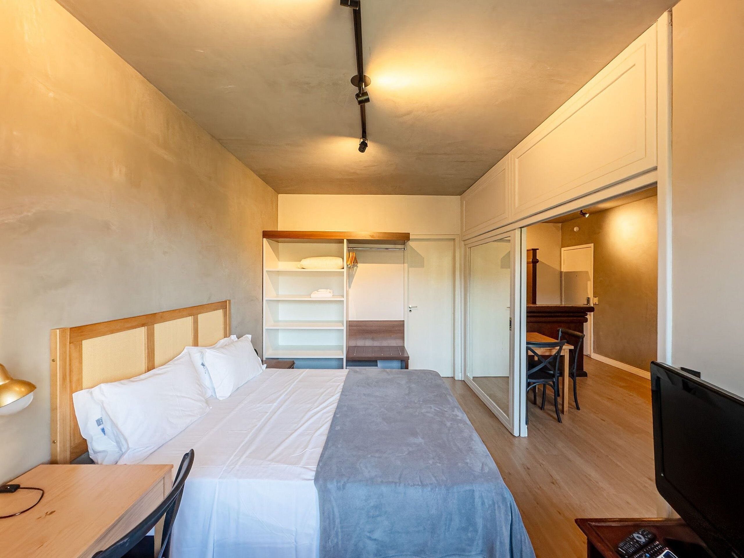 A hotel room with a bed, a desk, a chair, a TV, a wardrobe, and a mirror.