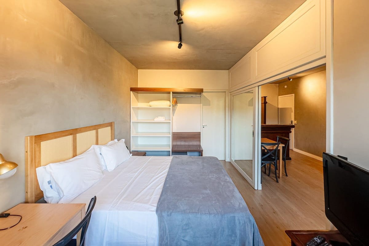 A hotel room with a bed, a desk, a chair, a TV, a wardrobe, and a mirror.
