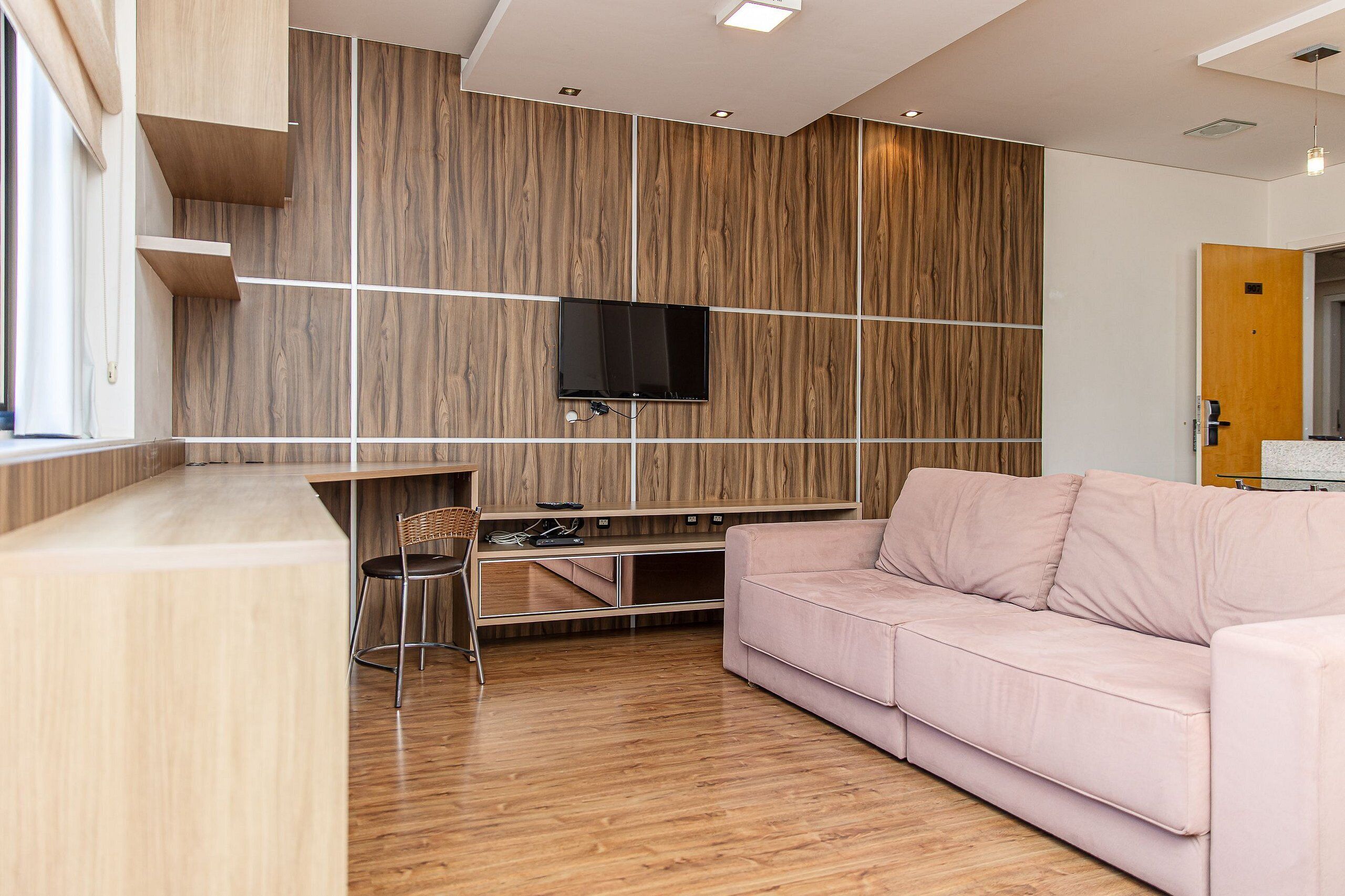 Una sala de estar moderna con una pared de acento de madera, un televisor de pantalla plana, un sofá rosa y una pequeña zona de comedor.