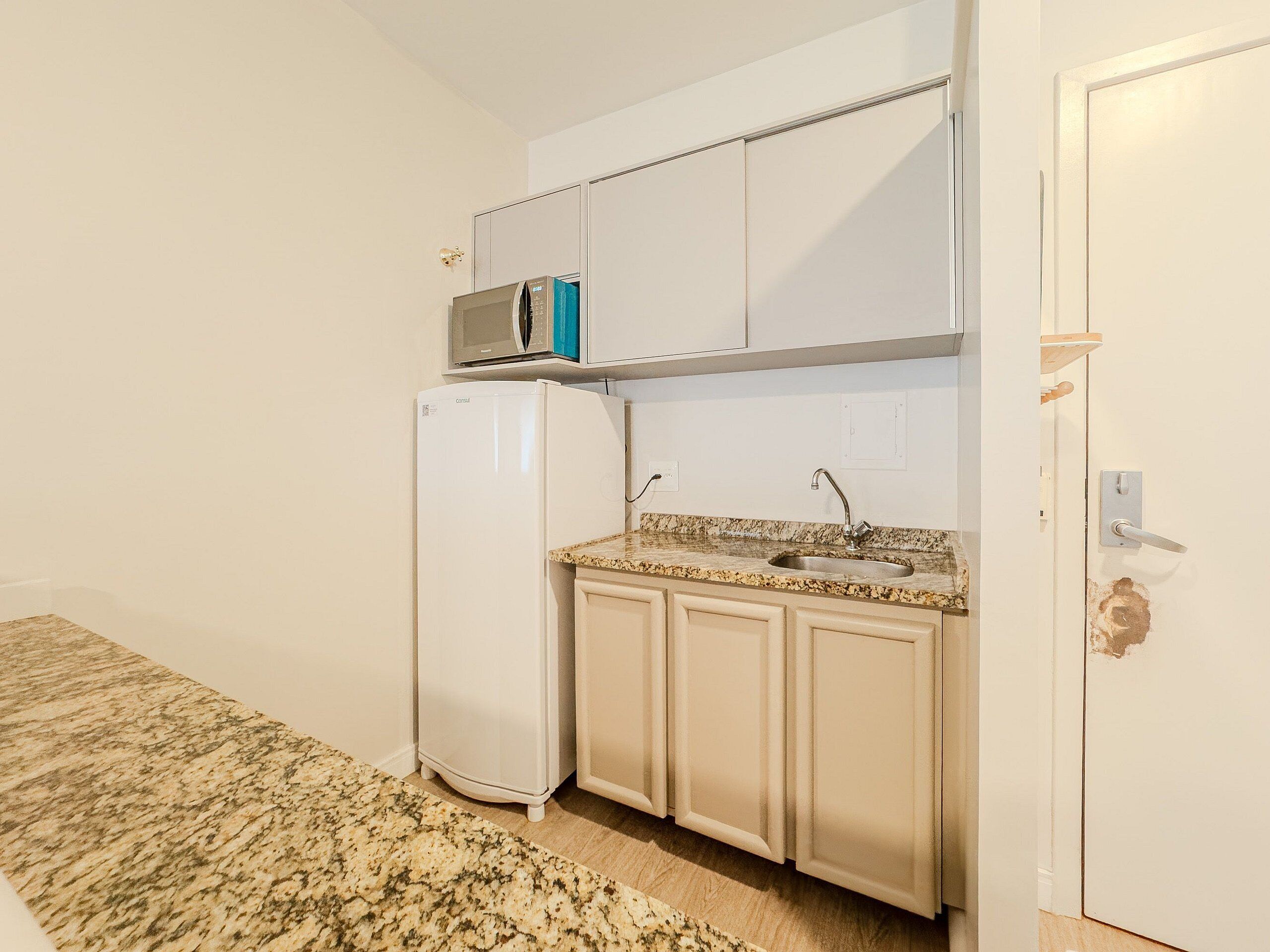Una cocina compacta con armarios blancos, microondas integrado, lavabo y refrigerador.