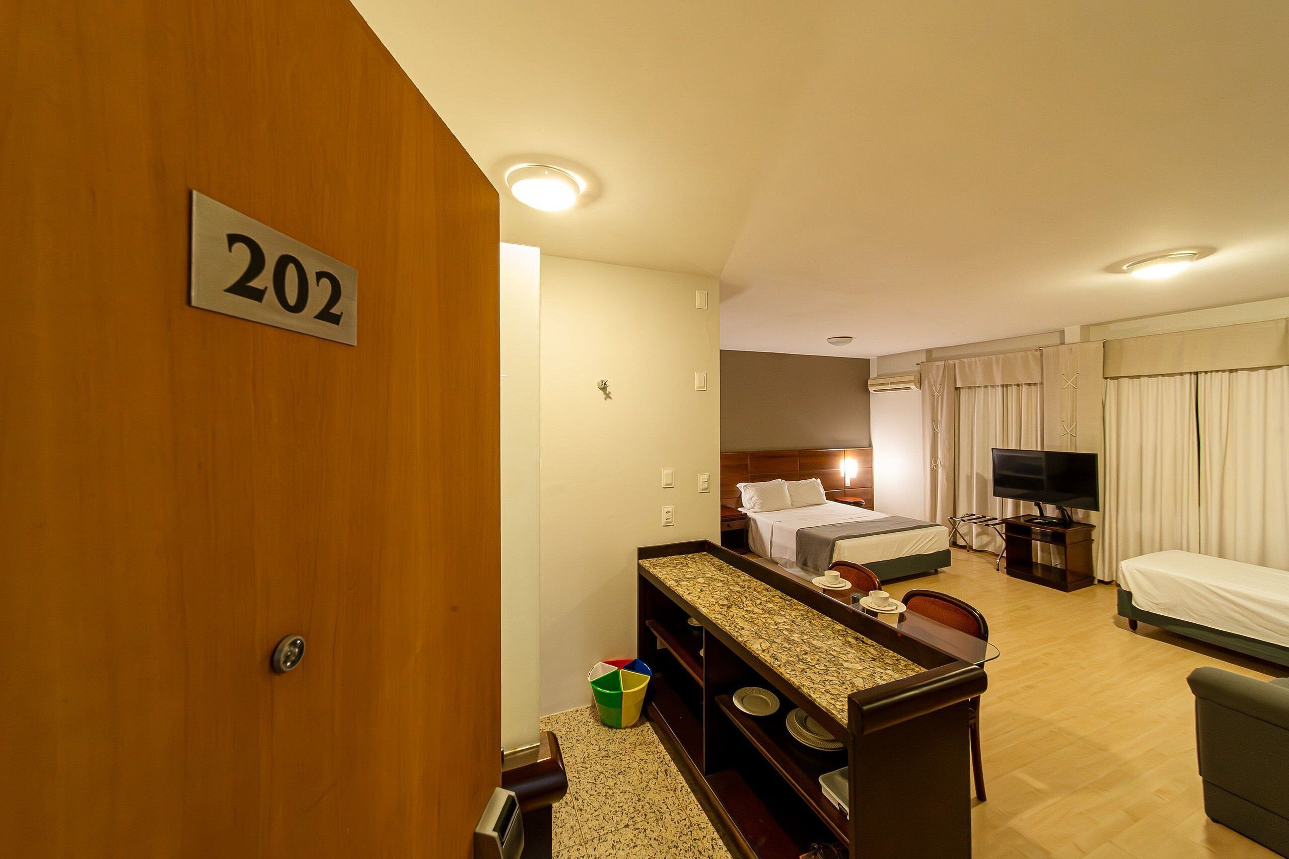 Habitación de hotel con cama, televisión, escritorio y letrero con el número 202 en la puerta.