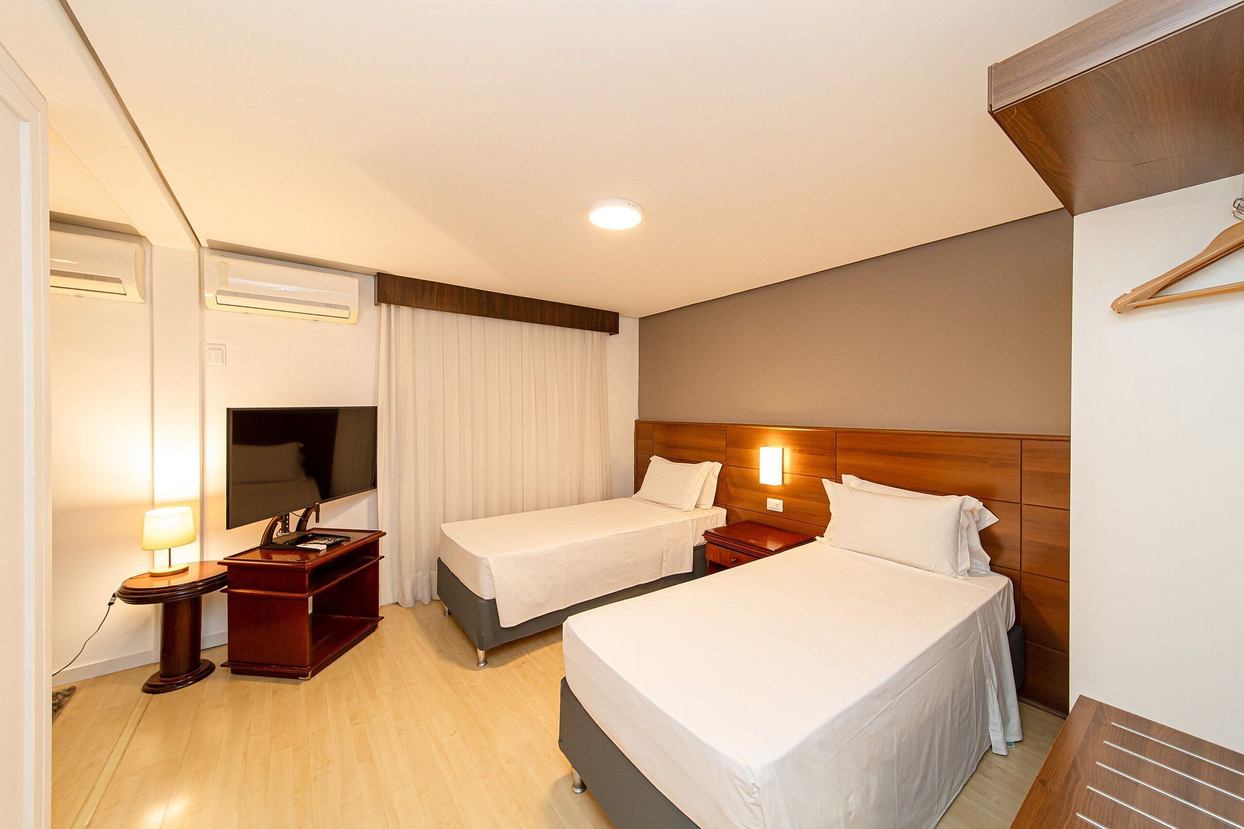 A hotel room with two beds, a desk with a lamp, a TV, and a wooden headboard.